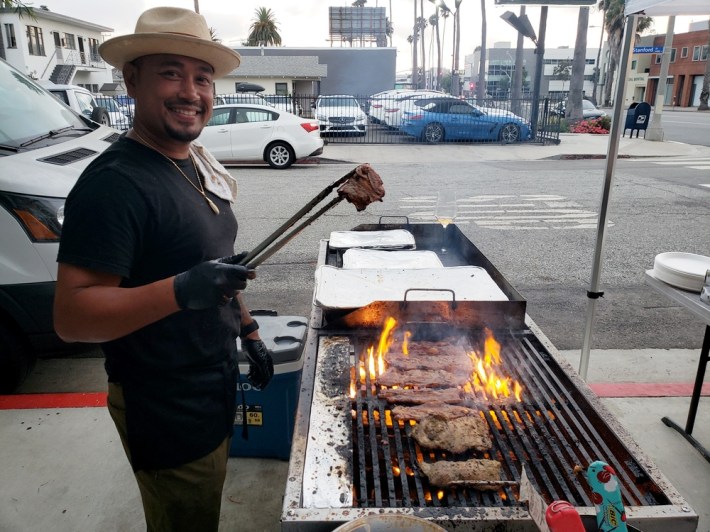 Sam Oum of Kreung Kitchen, holding a piece of meat with skewers over the grill